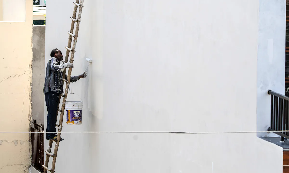 Exterior painter applying a fresh coat of paint from a ladder