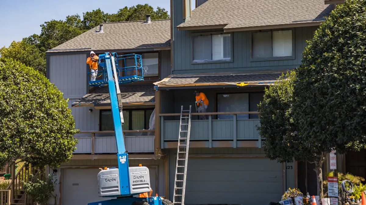 Exterior painting crew using ladders and a lift to reach a multistory home